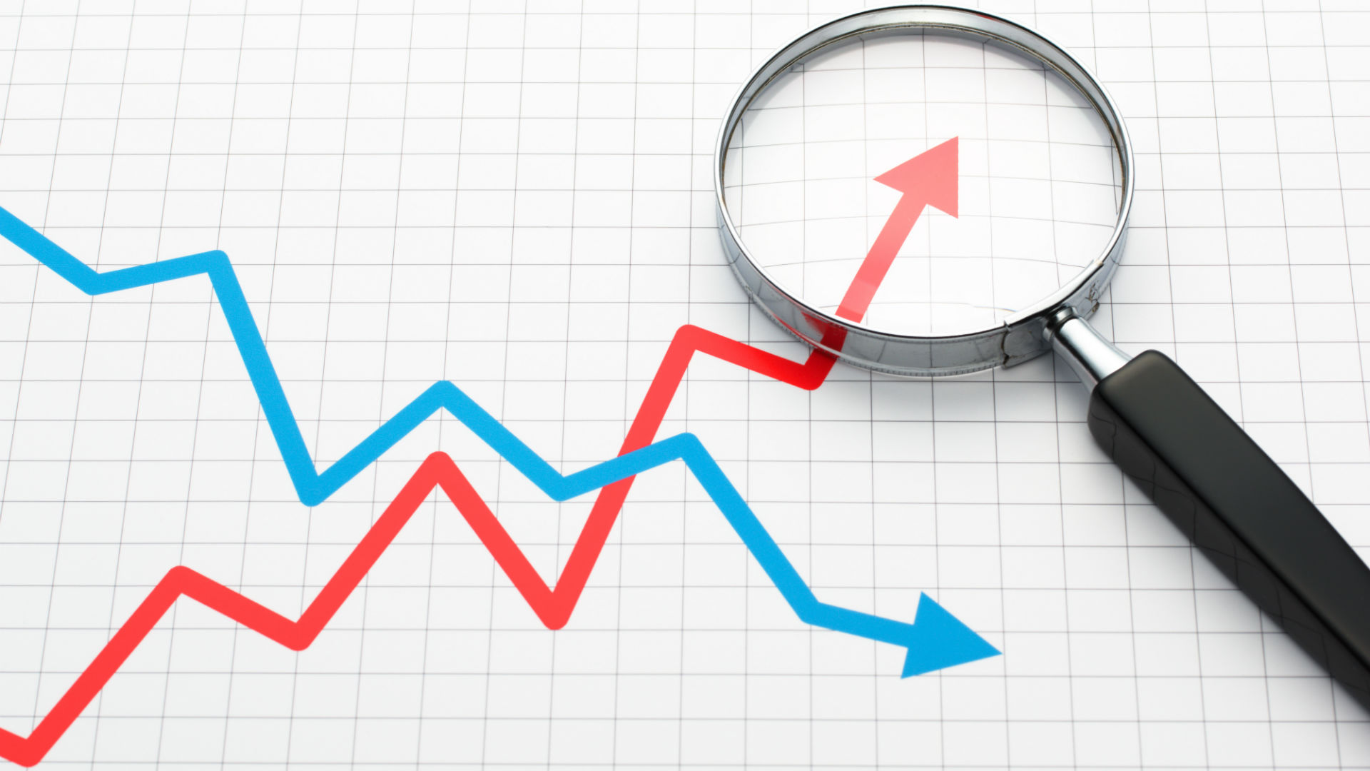  A magnifying glass sits on a graph showing business executives analyzing market trends represented by red and blue lines.